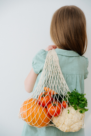 Back view. Closeup of a cotton bag with vegetables held by a caucasian redhead happy girlの写真素材