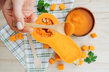 Closeup picture of spoon with porridge in hand on background parsley and fresh pumpkin slicesの写真素材