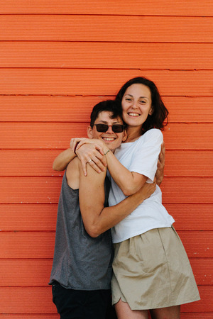 Happy handsome couple sharing their joy against orange house wall. Summer vacation memories.の写真素材