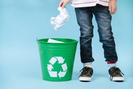 Little boy is throwing crumpled paper in green recycling bin. Croppedの写真素材