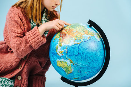 Happy modest teenage redhead girl looking for her home on a globe. Care about our planet. Recycling and ecology.の写真素材