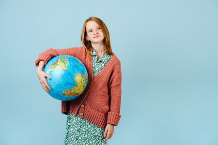 Happy modest teenage redhead girl holding earth globe under her arm. Care about our planet. Recycling and ecology.の写真素材