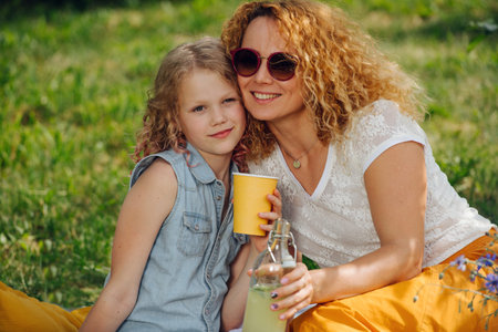 Summer family picnic on grass in the gardens. Mother in sunglasses and her teenage daughter, both...