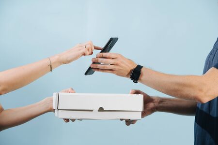 Woman hand is accepting a box delivery from a courier by signing on a smart phone. They both are holding the box, while she touches the screen. Cropped. Hands only.の写真素材