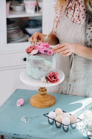 Close-up of girl's hands, she decorates cake with flowers while standing in the kitchen