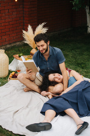 Middle-aged happy couple in love is reading a book together during a picnic on the lawn in their...