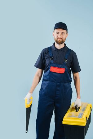 Portrait of confident service worker with saw and tool case, dressed in uniformの写真素材