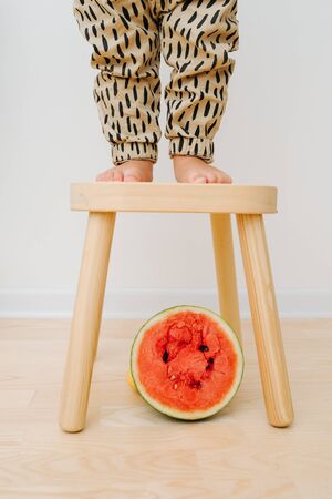 Little boys feet standing on stool. Red watermelon half slice is under it.の写真素材