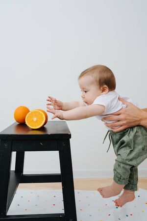 cute baby in his mothers hands trying to reach orangesの写真素材