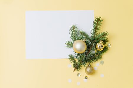 Happy new year minimalist composition. Sheet of paper, to write wishes, fir branch with golden christmas balls. Over yellow background, top view, flat lay.の写真素材