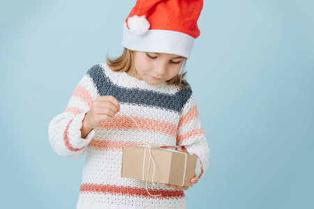Portrait of cute little first grader girl in a santas hat opening presentの写真素材