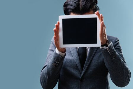 Businessman in a suit holding tablet over his face with screen outward over blueの写真素材