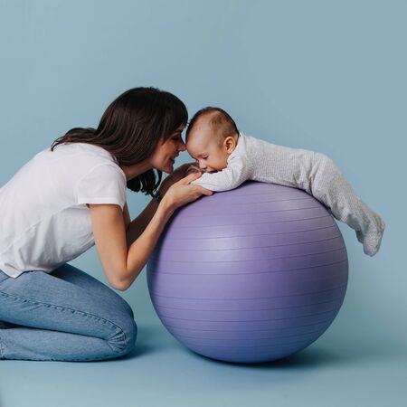 Happy mother doing exercises with her infant child baby on purple yoga ballの写真素材