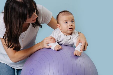 Happy mother doing exercises with her infant child baby on purple yoga ballの写真素材