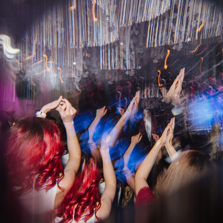 Young women on a concert clapping to the beat. Motion blur of hanging lamps, lights on stage and...