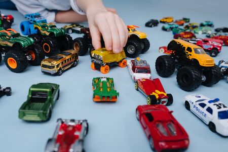 Little boy's hand playing with, moving one toy model car of many on the floor. Over blue background. Close up. Cropped, no face.の写真素材