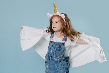 Toddler girl plaing in unicorn costume isolated on blue background