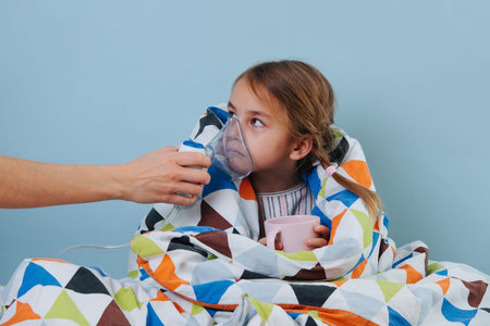 Sick girl with common cold sitting in bed under blanket with steam inhaler