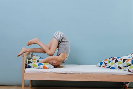 Little boy doing morning gymnastics in unmade bed. Forward roll exercise. Over blue walls. A way to strech and improve muscle strenghs and coordination.の写真素材
