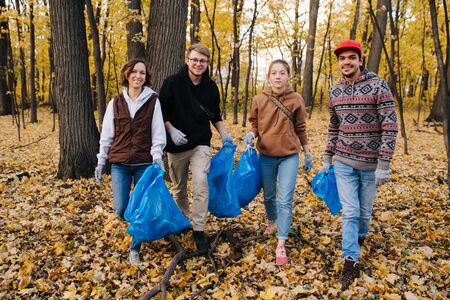 Group portrait of middle age volunteers posing with a trash bags in a seasonal forest at autumn, helping to clean forest floor from the litter. Two couples taking care of a park zone.の写真素材