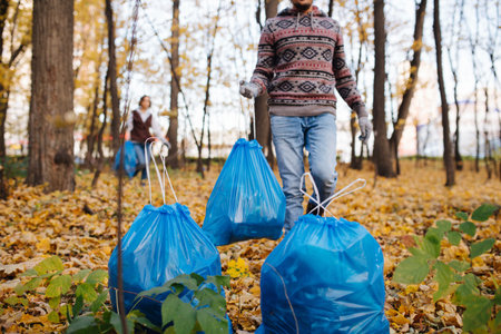 Middle age man bringing blue plastic trash bag to a pile. Volunteers collecting trash in a seasonal...