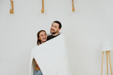 Portrait of a happy middle age couple wrapped up in a blanket. They just moved into a new apartment with no furniture. They are smiling, laughing.の写真素材