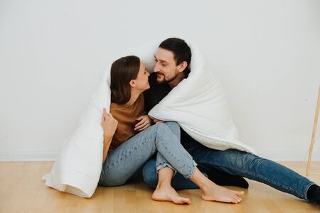 Portrait of a middle age couple sitting on the floor wrapped in a blanket, about to kiss. They just moved into a new apartment with no furniture. Both happy. Dressed casually.の写真素材