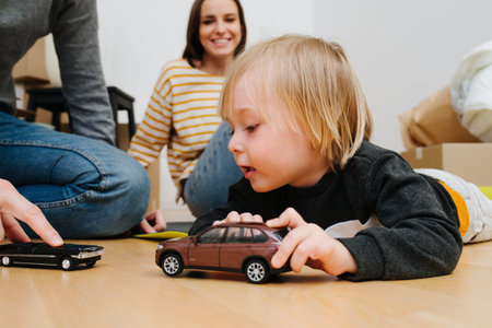 Young family moving into a new apartment. Father and son play with model toy cars on the floor...