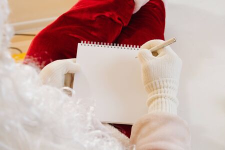 Close-up. Santa Claus hands in white gloves writing a letter in a notebook. Place for textの写真素材