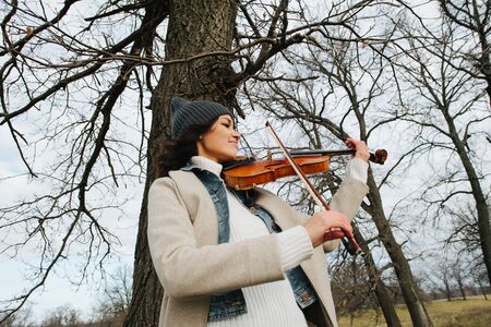 Warmly dressed woman playing violin in a countryside at autumnの写真素材