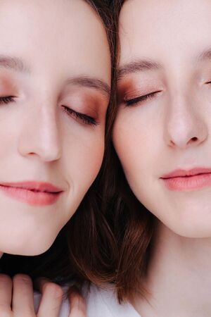 Close-up of two faces of twin sisters with nude make-up. They are posing with their eyes closed.の写真素材