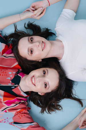 Female friendship of two twin sisters, holding each other's hands lying on the floor, top view