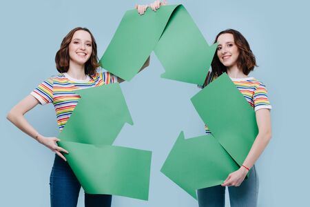 Girls twin sisters holding a symbol of recycling in their hands. Protection of the environment conceptの写真素材