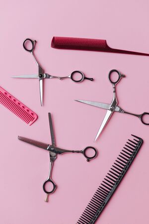 Composition of three pairs of metal hairdresser scissors placed in an equally open position and three professional combs over pink background. Here are all-purpose shears and blending shears. Top viewの写真素材