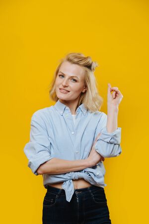 Portrait of an attractive blonde woman with a curious look in a belly-tied jeans shirt over yellow background.の写真素材
