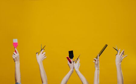 Three sets of woman hands in the air holding hairdresser tools, such as brushes, scissors and combs over yellow background.の写真素材