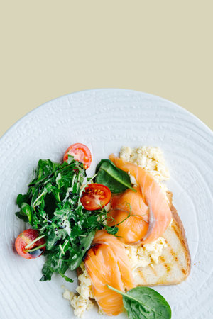 Salted salmon, scrambled eggs on toast with spinach and tomato salad served on a white plate. Top...