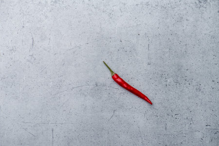 Long shot of a single small red chili pepper on a grey stone surface background with dotted and...