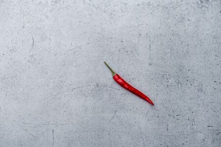 Long shot of a single small red chili pepper on a grey stone surface background with dotted and scraped texture.の写真素材
