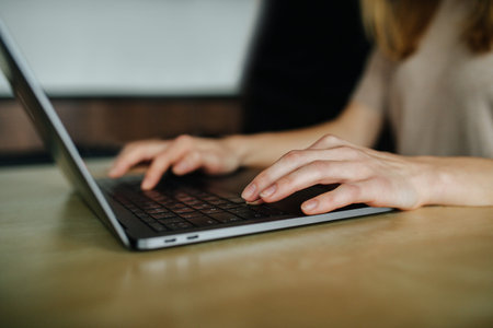 Hands of a female freelancer, working behind the table at home. She's typing something on a laptop...