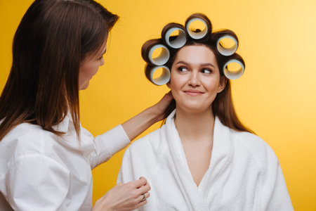 Woman in a beauty salon sits with hair in rollers, being comforted by staffの写真素材