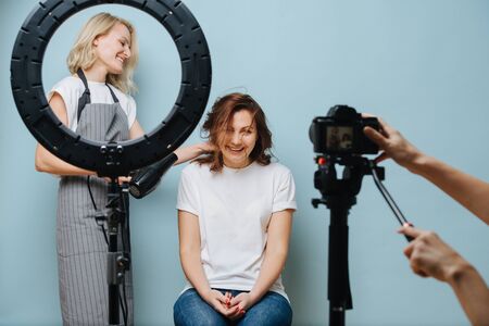 Happy female stylist drying clients brown hair while photo is takenの写真素材