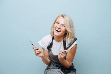 Cheerful blonde hairdresser woman with combs and scissors in handsの写真素材