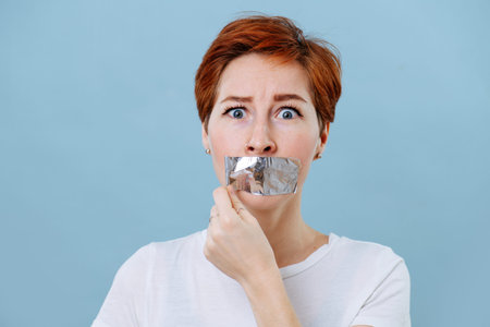 Portrait of a frightened middle aged woman with short ginger hair and her mouth scotch taped....