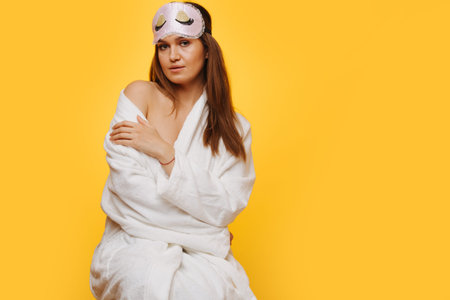 Insecure brunette woman in a bathrobe with bare shoulder sitting on a stool, looking at camera....