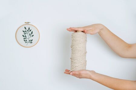 The girl's hands hold a cotton rope for the macrame, against the background of the white wall and embroideryの写真素材