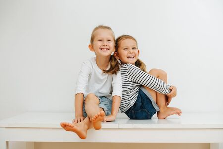 emotional portrait of 5 and 7 year old blond sibling sitting at home on a tableの写真素材