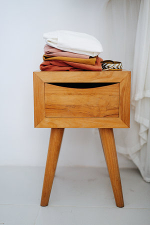 Multi-color folded dresses and bracelets on an old wooden bedside table. Frontal view.