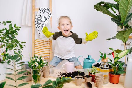 Little boy in gardening gloves grimacing, fooling around, yelling, making scary face. All that to lift the boredom from having to work with plants.の写真素材