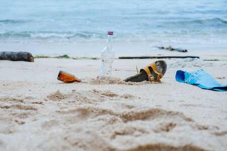 Garbage composition digged in a white sand beach of a polluted ocean shore. Glass bottles, shoe and covering piece.の写真素材